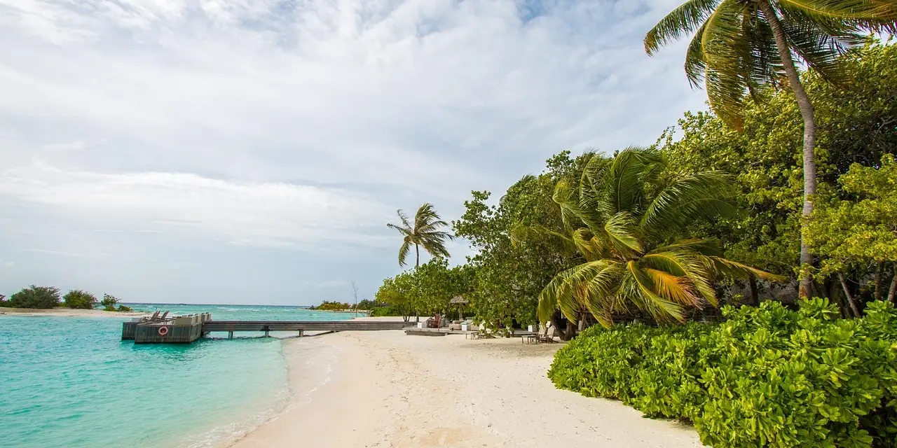 Plage de sable blanc, ponton et lagon turquoise à Kuda Huraa, aux Maldives